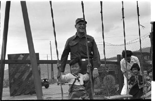 Man behind two small children on swings