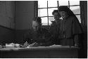 Man at a desk and a nun standing behind him