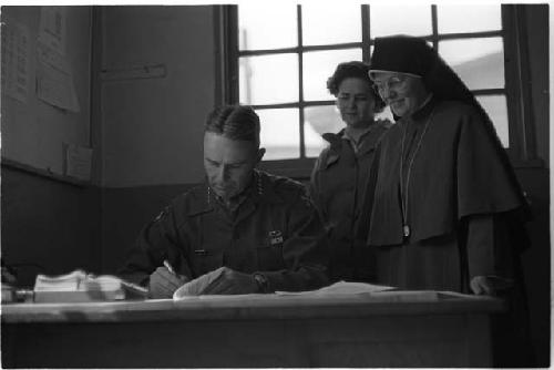 Man at a desk and a nun standing behind him