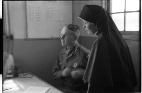 Man sitting down and a nun standing next to him