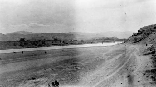 Scattered people walking along shore toward distant bridge