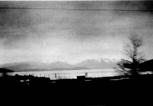 Scene with buildings on lake shore, distant mountains