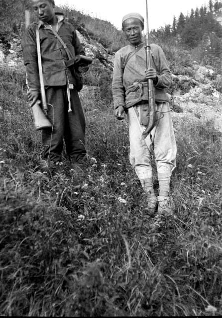 Two chinese men standing on hillside holding rifles