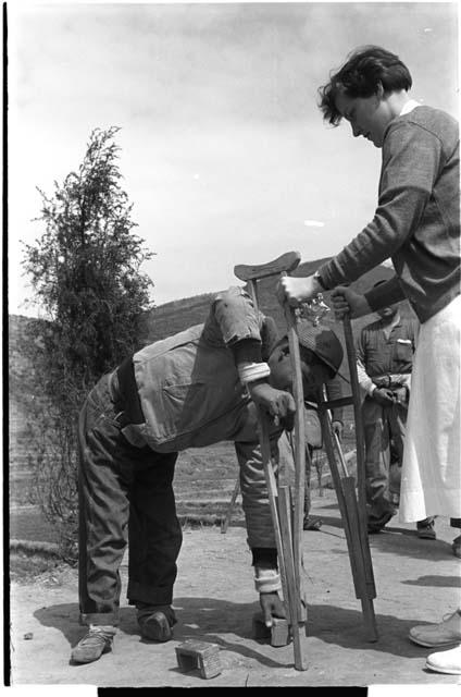 Woman holding crutches while a boy bends over to the ground