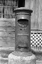 Tall metal structure on sidewalk, possibly a mailbox.