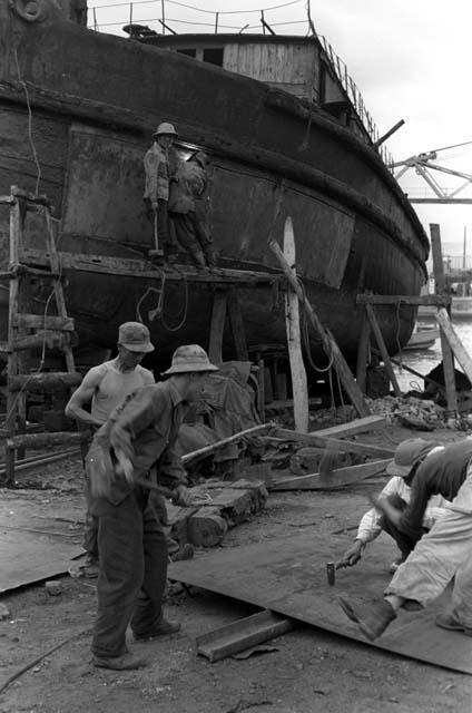 Men working on boards/structure in front of docked ship.