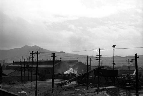 Shot of warehouse area, many electrical wire poles; mountain in background.