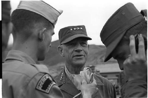 Man in military uniform speaking into a microphone with four stars on his cap