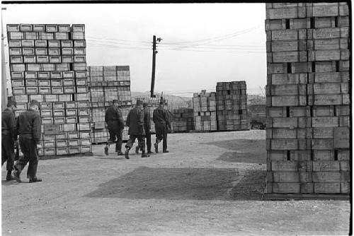 Military personnel walking between stacks of supplies