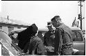 Two men speaking with a nun beside a parked car