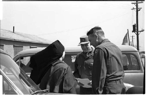 Two men speaking with a nun beside a parked car