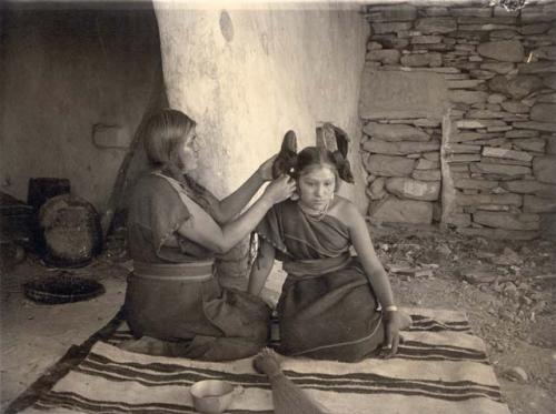 Two Hopi women, one giving the other the squash-blossom hairstyle