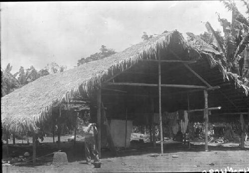 Man with rifle in front of thatched hut