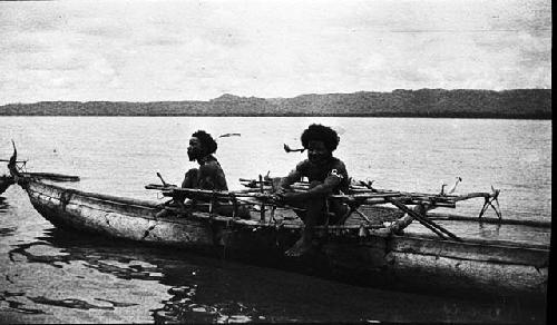 Two men in canoe with feathers in their hair