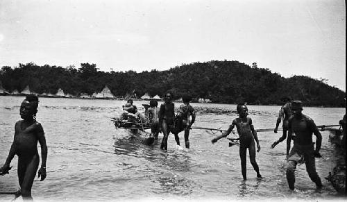 View of triangular homes behind men wading in river with boat