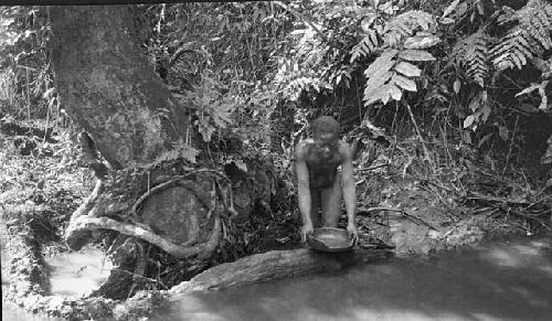 Woman collecting water from stream in bowl