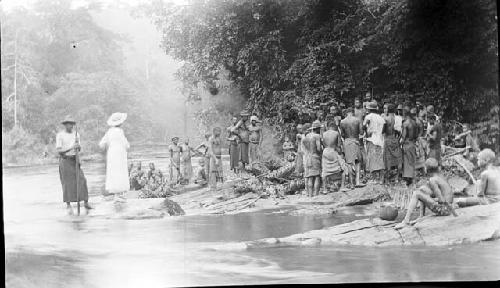 Group gathered near stream with cut plant material and baskets