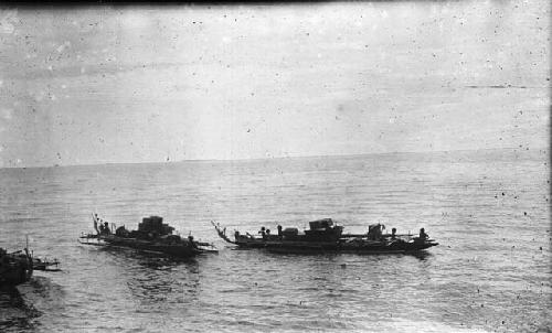 Men riding in a double outrigger dugout canoe with cargo