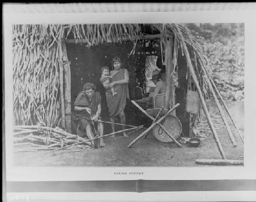 Man making arrows with woman and child