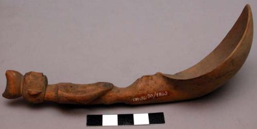 Wooden spoon, handle carved in human effigy: hands resting on flexed knees, sadd