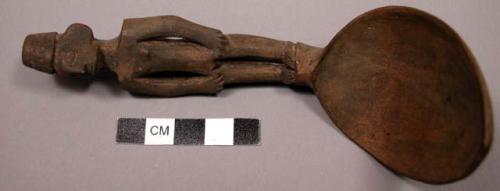 Wooden spoon, handle carved in human effigy: hands resting on flexed knees, fema