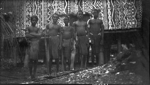 Men in front of decorated hut on stilts with intricately painted facade