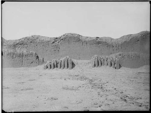 Truncated portico of a small plaza opening on narrow winding passage. Background is encircling wall of northeastern side of the Bandelier Group.