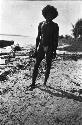 Man in loin cloth on beach in front of canoe