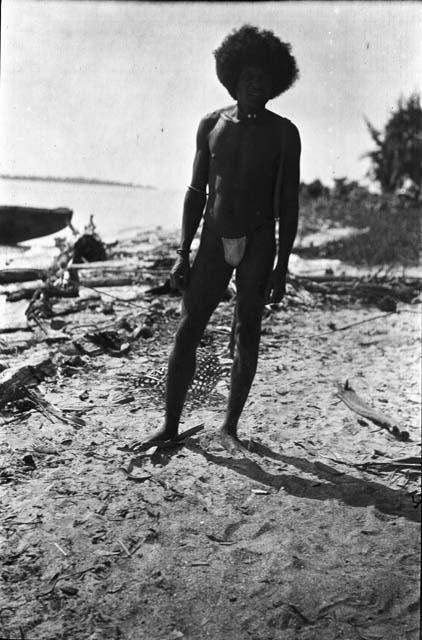 Man in loin cloth on beach in front of canoe