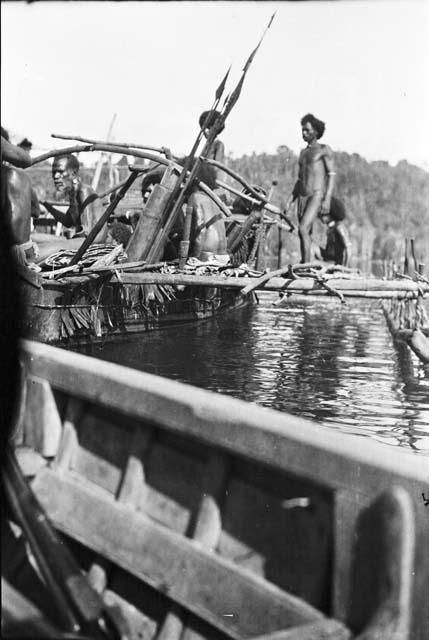 Men rowing a double outrigger dugout canoe with armaments