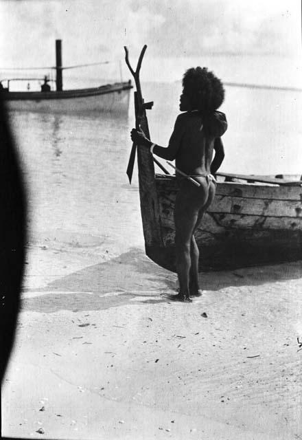 Man standing on shore with dugout canoe