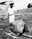 Stone sculpture of large seated pot-bellied figure, man standing behind