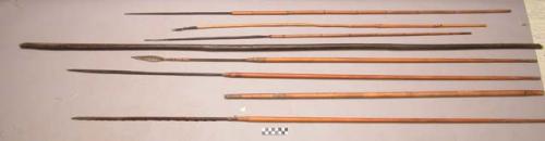 8 wooden arrows, some with carved points, 1 bow, 1 arrow with metal point.