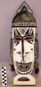 Wood mask painted white, black, and red with brush-like dried reed +