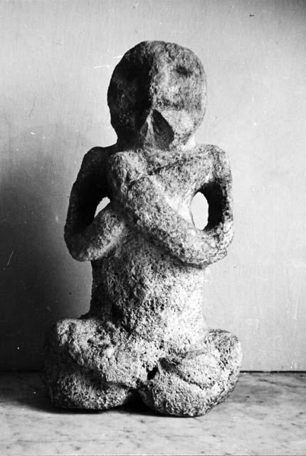 Crude stone figure, seated with crossed arms and legs