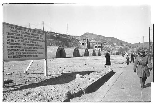 Temporary Quonset huts next to "Pusan Rehabilitation and Reconstruction Program" sign