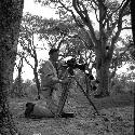 Robert Gardner kneeling next to his camera and tripod, preparing to film