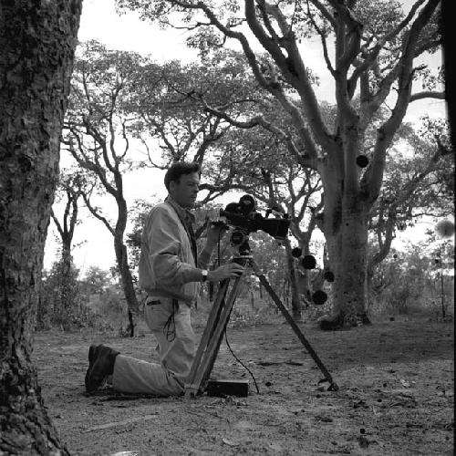 Robert Gardner kneeling next to his camera and tripod, preparing to film