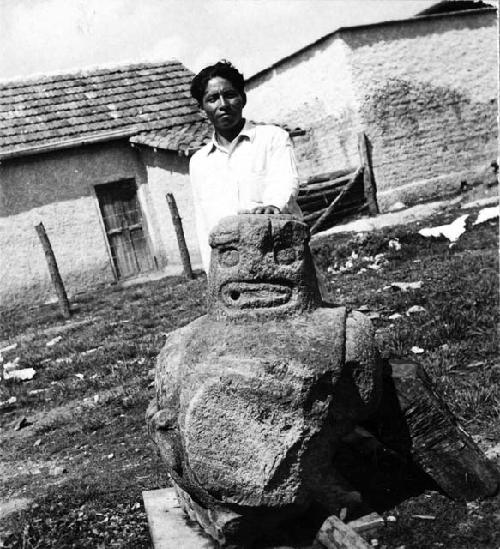 Stone sculpture of large seated pot-bellied figure, man standing behind