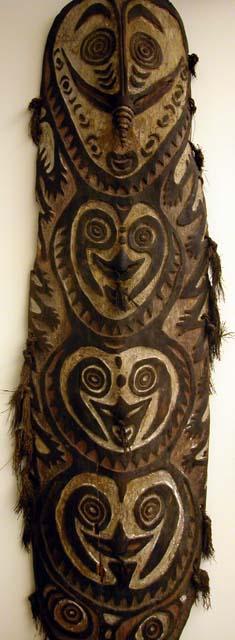 Carved wooden shield, painted and decorated with grass