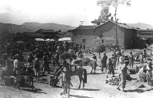 People and horses near a building, pots on the ground