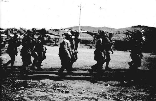 Soldiers marching through field with guns on their shoulders