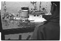 View of sinking U.S. Army tugboat over man's shoulder
