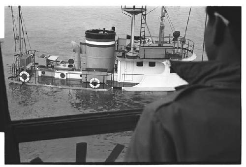 View of sinking U.S. Army tugboat over man's shoulder