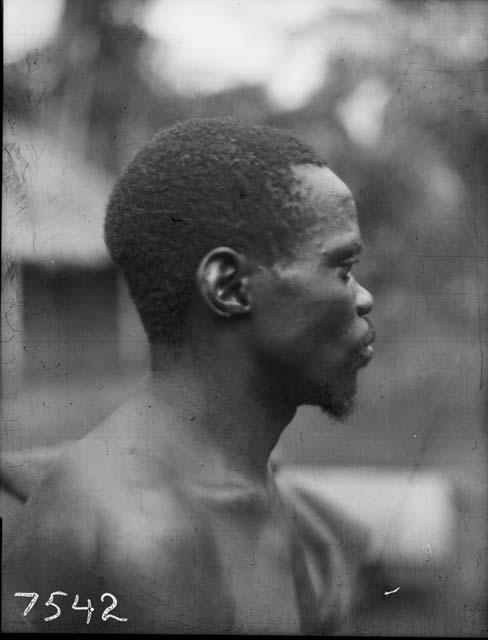 Frontal view of Karu male with chest scar tattooing in front of hut