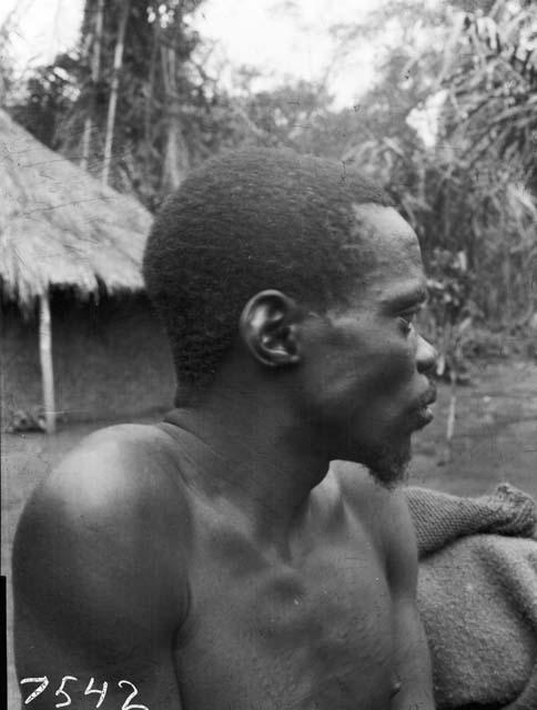 Frontal view of Karu male with chest scar tattooing in front of hut