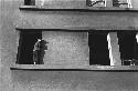 Boy standing on building window ledge.