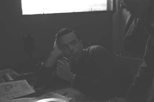 Military man with pipe in mouth sitting at desk.