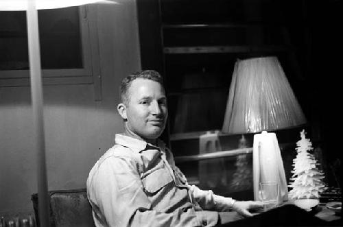 Man sitting in chair next to a lamp and a little tree.