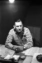 Military Man (Earl L. Denton name tag) sitting at desk, holding a cigarette.